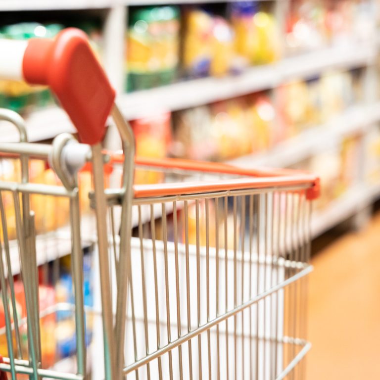 Shopping trolley cart with shallow DOF against modern supermarket aisle blurred background